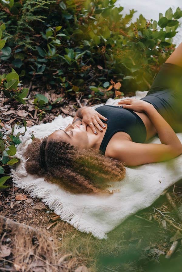 pexels photo 8981327 A woman with curly hair meditates on a white towel amidst greenery outdoors, embracing nature.