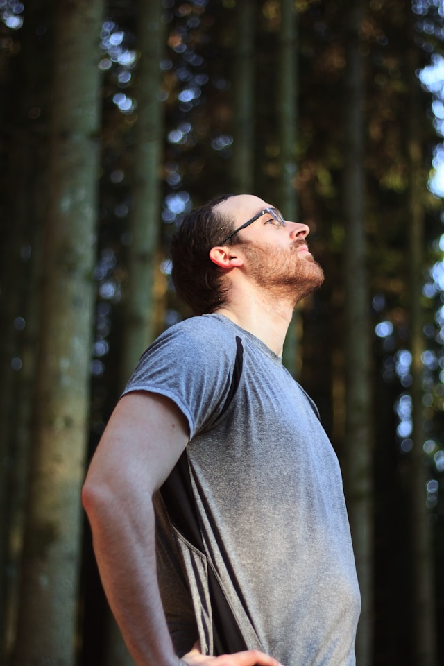 Breathwork in Bewegung: Ein Mann im T-Short steht im Wald und schaut nach oben in die Sonne